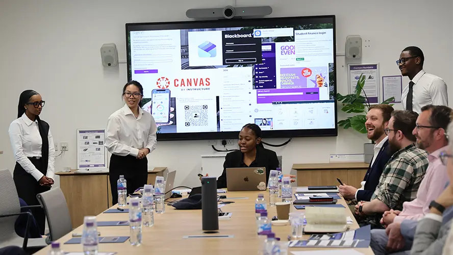 Four ITMB students presenting to a boardroom of university representatives and industry professionals.
