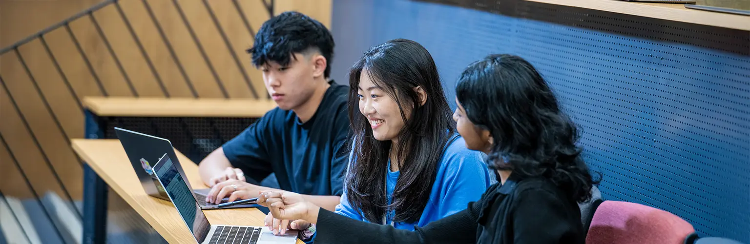 Three students sitting in a lecture theatre working on laptops.