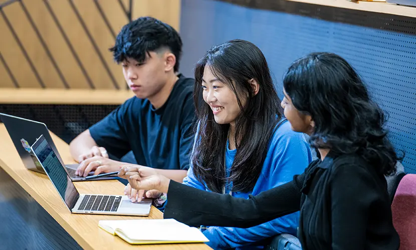Three students sitting in a lecture theatre working on laptops.
