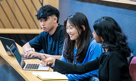 Three students sitting in a lecture theatre working on laptops.