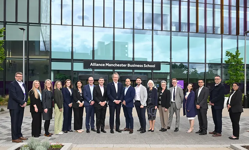 A large group of representatives from the University of Manchester executive, Alliance MBS, Unit M, and BNY standing in front of Alliance MBS building.