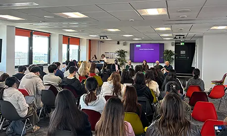 An event with rows of chairs full of students and a panel of five people speaking at the front of the room.