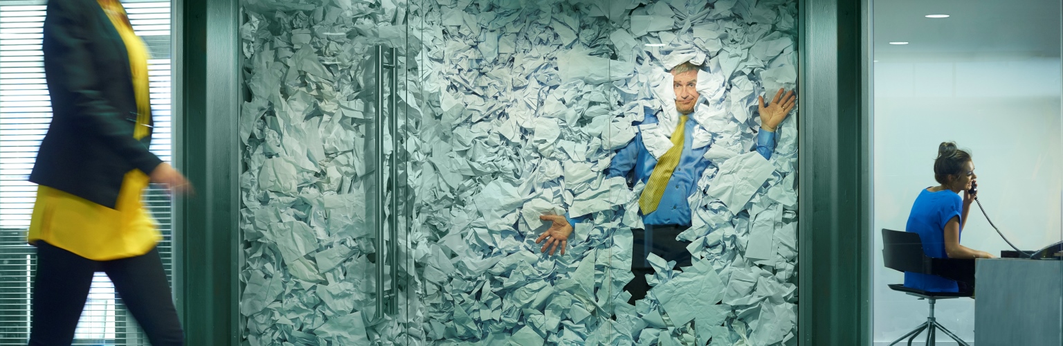 man squashed in office with too much paper