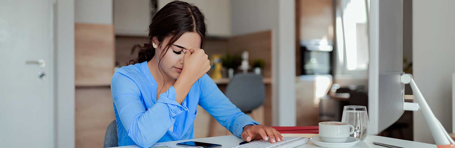 A woman in a blue top stressed at her office desk