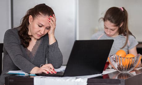 A woman looking stressed at home on her laptop 
