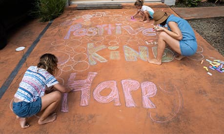 A family colouring in a road with the words 'happy', 'kind' and 'positive'