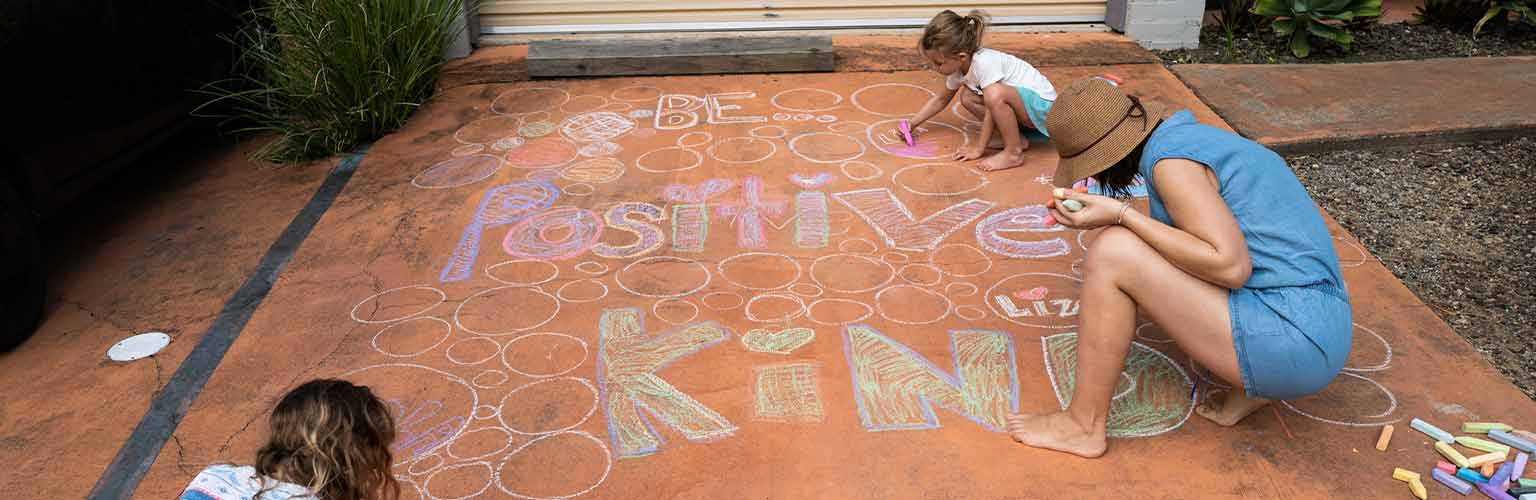 A family colouring in a road with the words 'happy', 'kind' and 'positive'