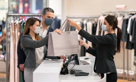 A female retail worker handing over a bag of shopping to a female customer with a facemask on.