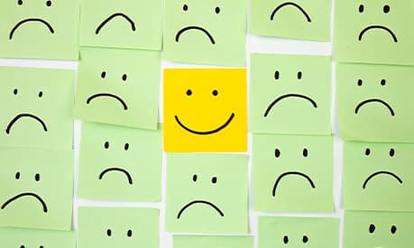 a post-it note with one happy face compared to all the sad faces surrounding it