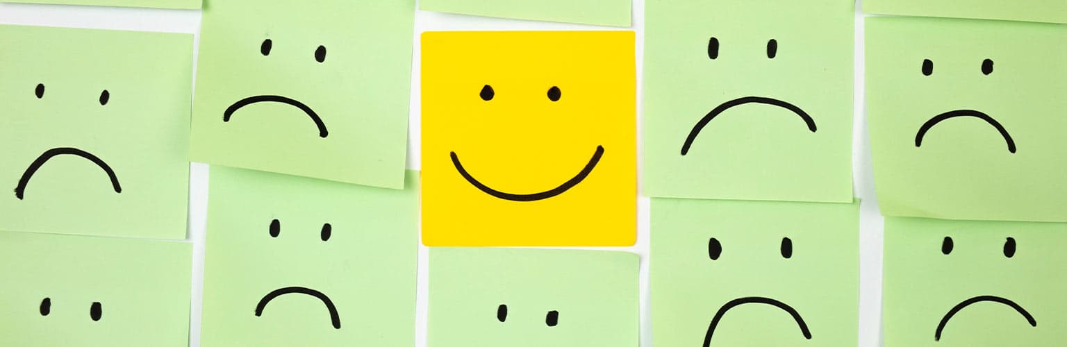 a post-it note with one happy face compared to all the sad faces surrounding it