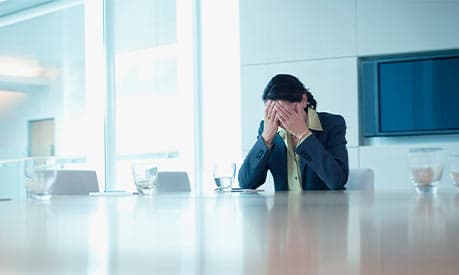 A woman sitting in a boardroom with her hands on her face