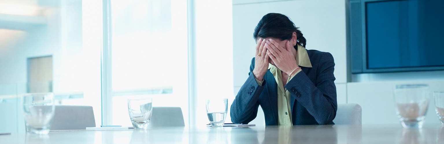 A woman sitting in a boardroom with her hands on her face