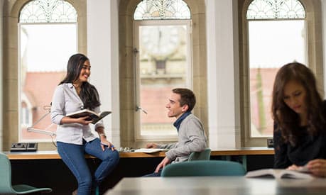 Two students smiling one one holds a book