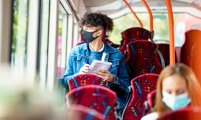 A man sitting on a public bus wearing a black face mask