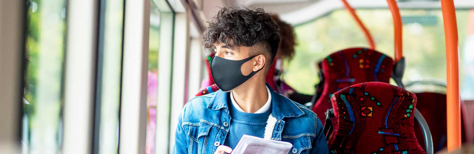 A man sitting on a public bus wearing a black face mask