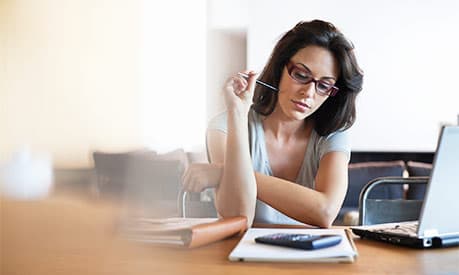 A woman holding a pen looking at her notebook at a desk