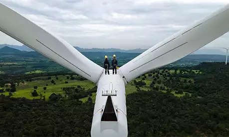 two people standing on top of a wind turbine