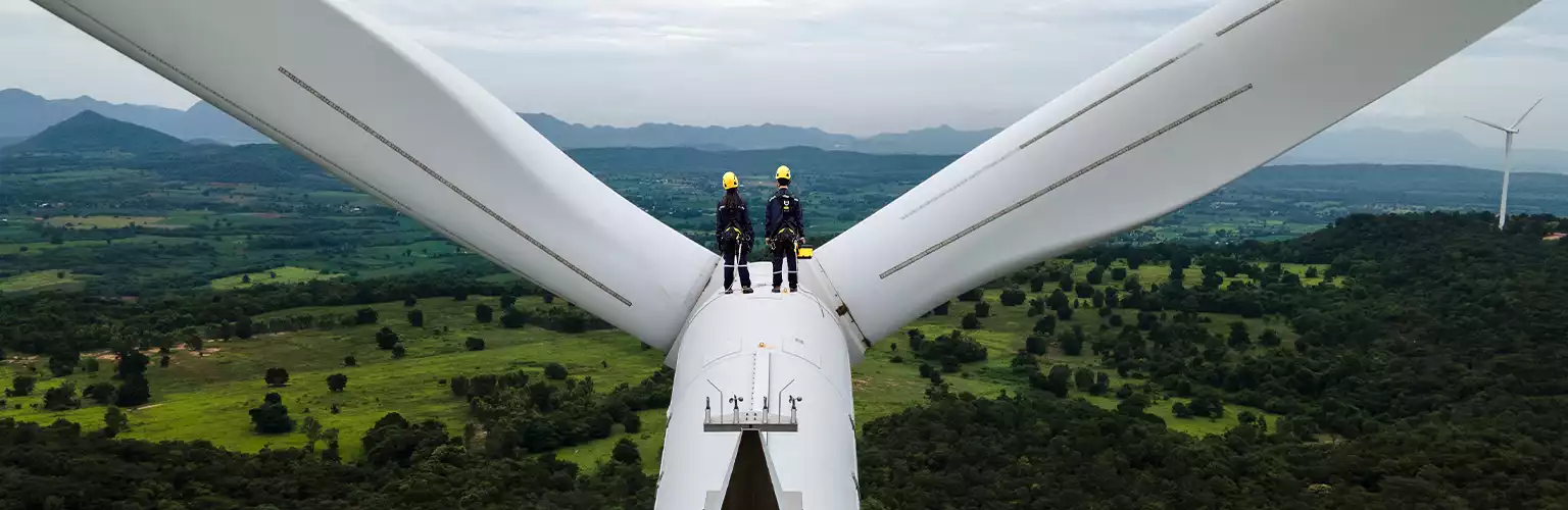 two people standing on top of a wind turbine