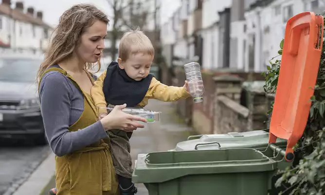 A woman showing a toddler how to recycle a plastic bottle
