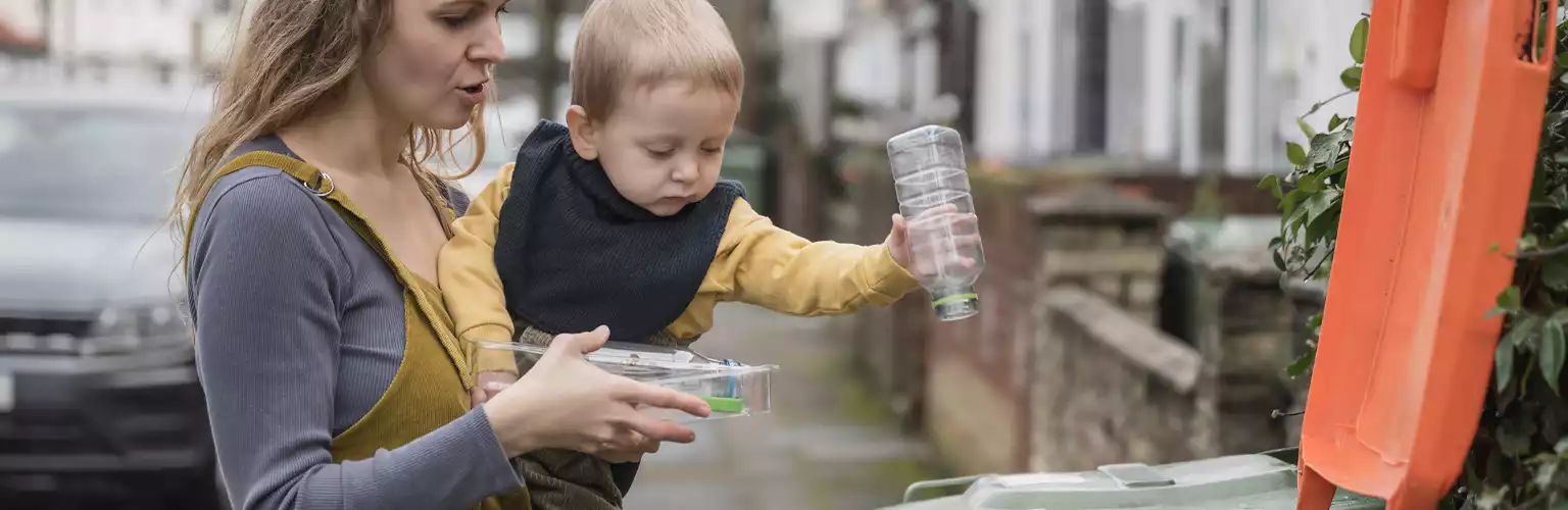 A woman showing a toddler how to recycle a plastic bottle