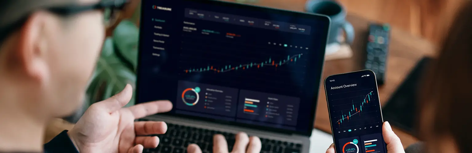 Two people working on a laptop and a smartphone looking at data