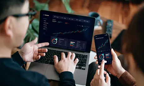 Two people working on a laptop and a smartphone looking at data