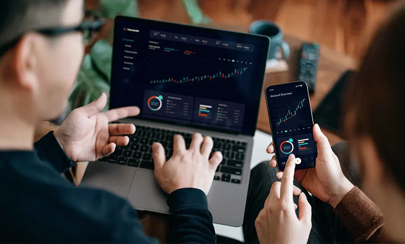 Two people working on a laptop and a smartphone looking at data