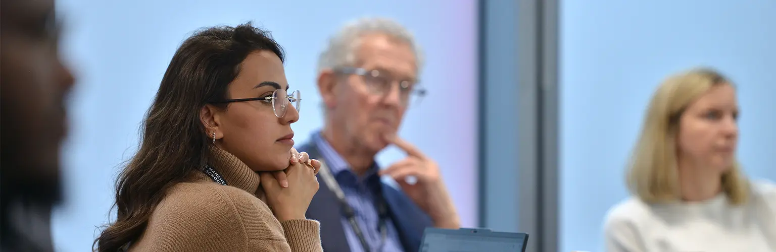 A group of professionals sitting around a table listening to someone at the front of the classroom speak