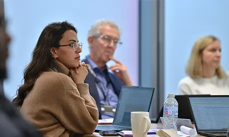 A group of professionals sitting around a table listening to someone at the front of the classroom speak