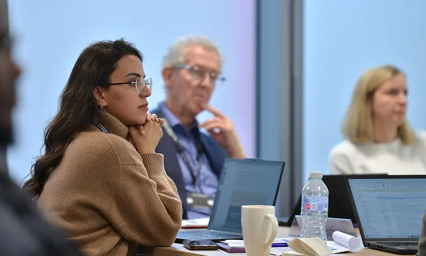 A group of professionals sitting around a table listening to someone at the front of the classroom speak