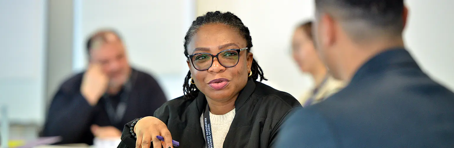 A professional woman sitting in a classroom environment talking to a peer