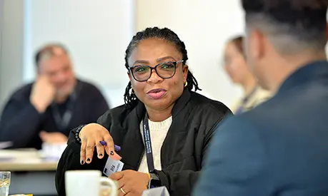 A professional woman sitting in a classroom environment talking to a peer