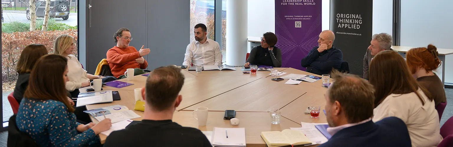 A group of around 12 business leaders sat around a round table in conversation with each other