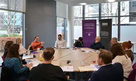 A group of around 12 business leaders sat around a round table in conversation with each other