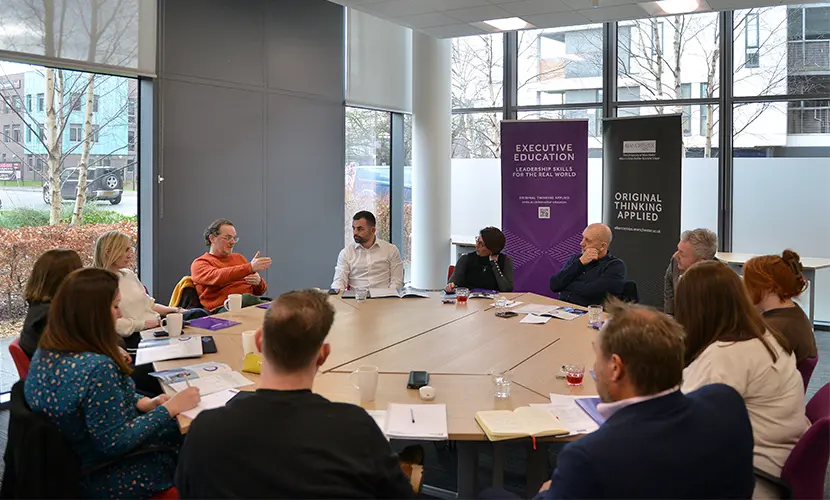 A group of around 12 business leaders sat around a round table in conversation with each other