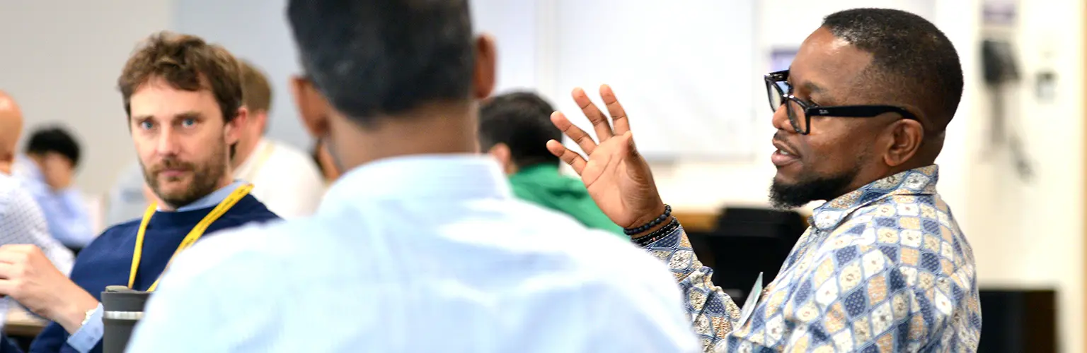 Three male professionals sitting together in a classroom environment talking amongst one another