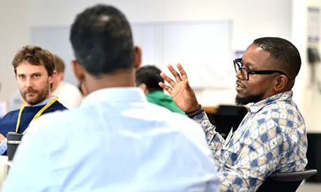 Three male professionals sitting together in a classroom environment talking amongst one another