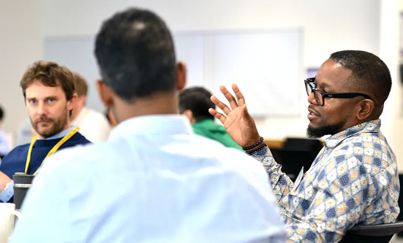 Three male professionals sitting together in a classroom environment talking amongst one another