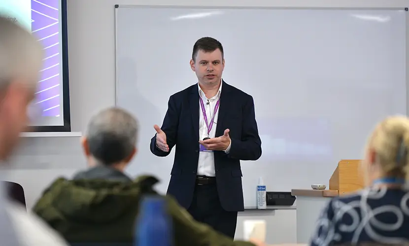 A professional academic stood at the front of a classroom delivering a session to a room of senior leaders
