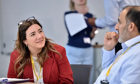 Two professionals sat at a table chatting to one another in a classroom environment