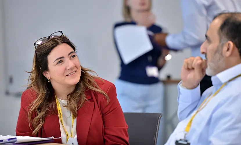 Two professionals sat at a table chatting to one another in a classroom environment