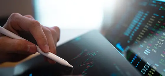 A person looking at finance data on a monitor and interacting with data on a tablet.