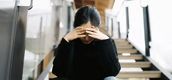 A young Asian white-collar worker, wearing a black overcoat, was sitting sadly on the stairs.