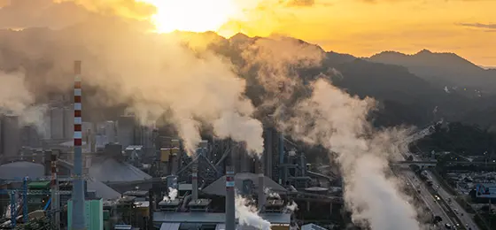 A sprawling industrial factory emits thick smoke under a vibrant golden sunset, highlighting environmental concerns and pollution issues.