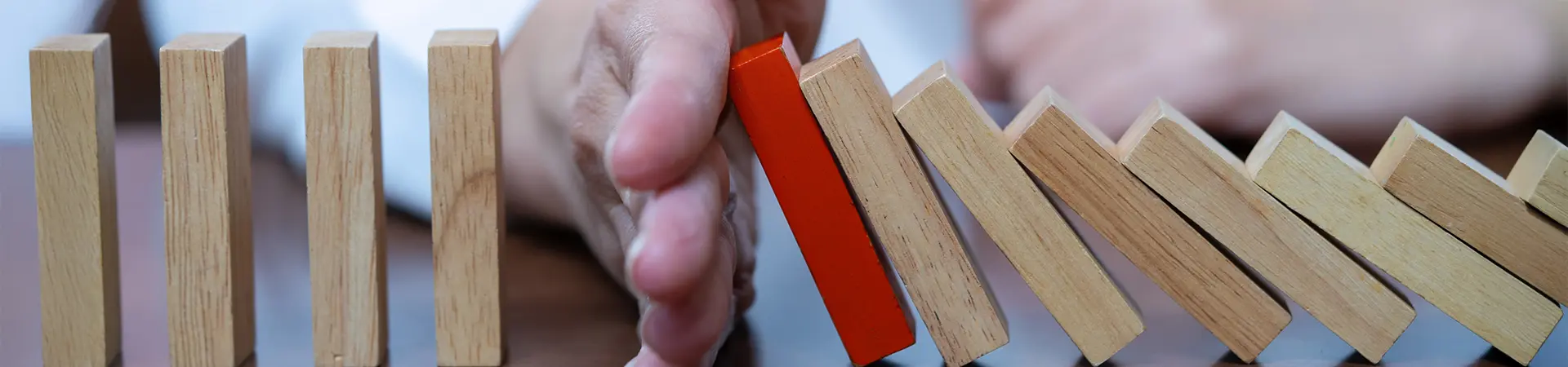 Wooden dominoes in a row with a person's hand in the middle stopping them from falling.