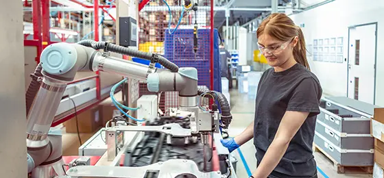 Female worker working with a robotic assembly machine in automotive parts factory.