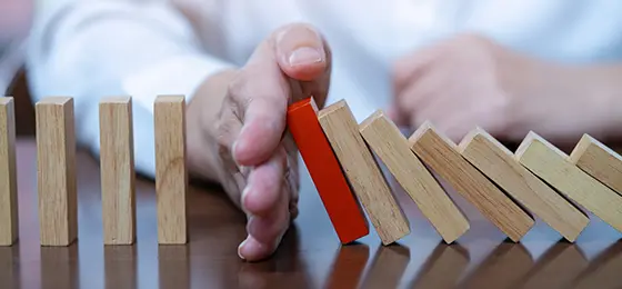 Wooden dominoes in a row with a person's hand in the middle stopping them from falling.