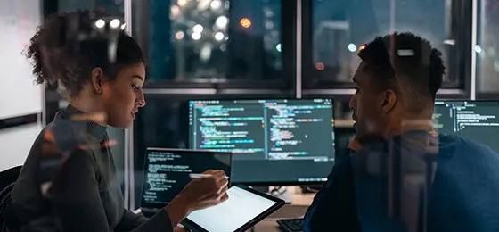 Two Software developers in modern office collaborating analysing the coding on computer screen.