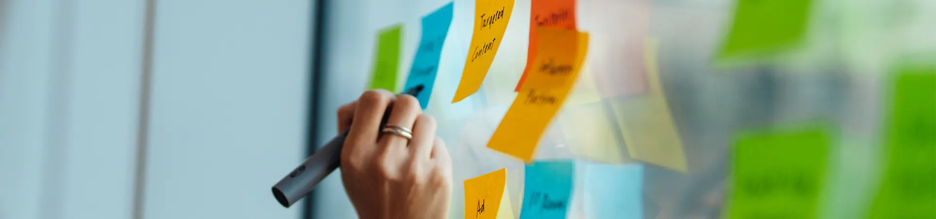 A woman writing on sticky notes displayed on an office window.