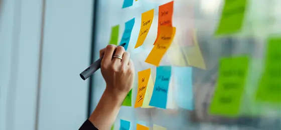 A woman writing on sticky notes displayed on an office window.